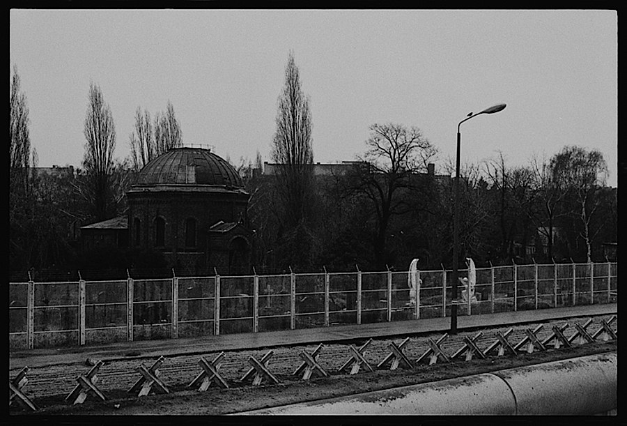 Photographie noir et blanc d'un cimetière coupé en deux par le mur de Berlin