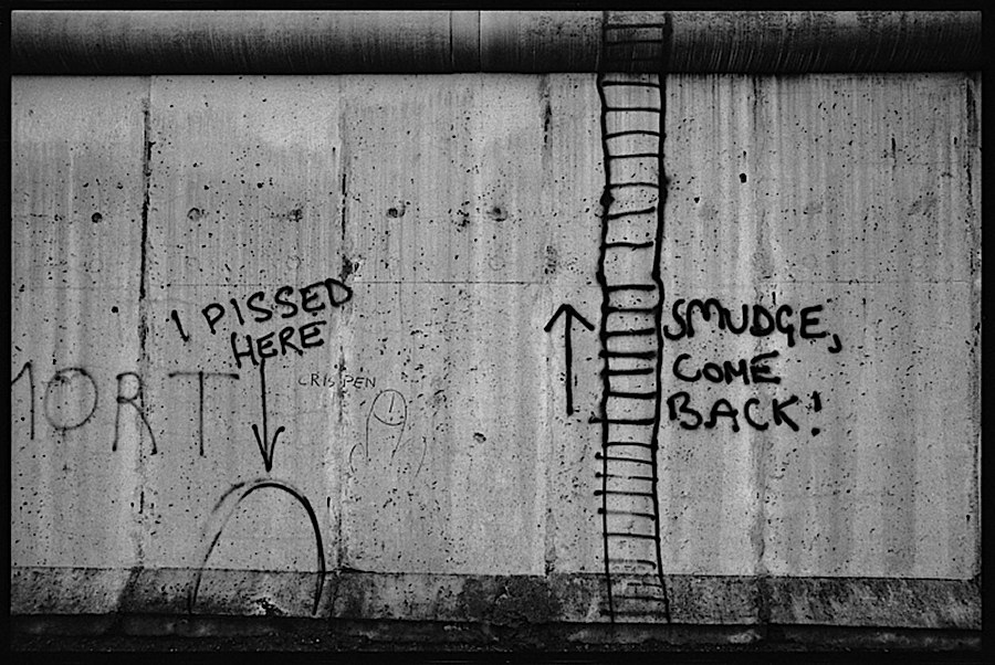 Photographie noir et blanc de differents graffitis dont les mots 'I pissed here', une échelle grossiérement réalisée et un autre message 'smudge, come back'
