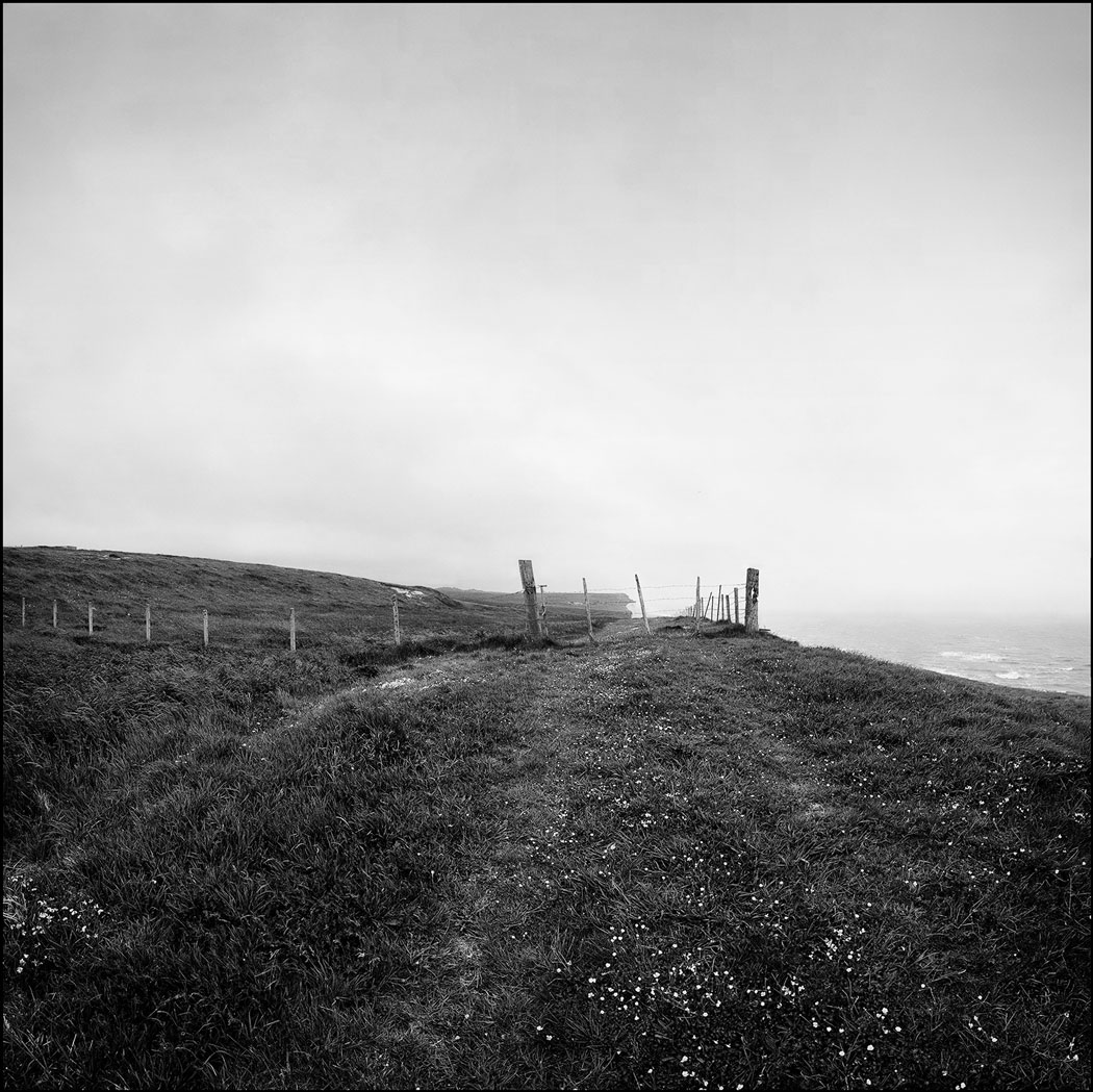 Photographie numérique d'un bord de falaise avec une barrière vers un champ